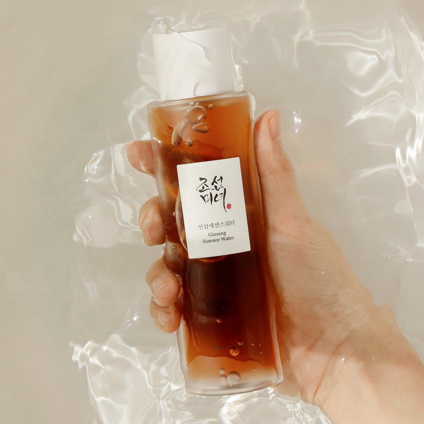 K-Beau's model hand holding Ginseng Essence Water in water backdrop – premium Korean beauty hydration treatment.
