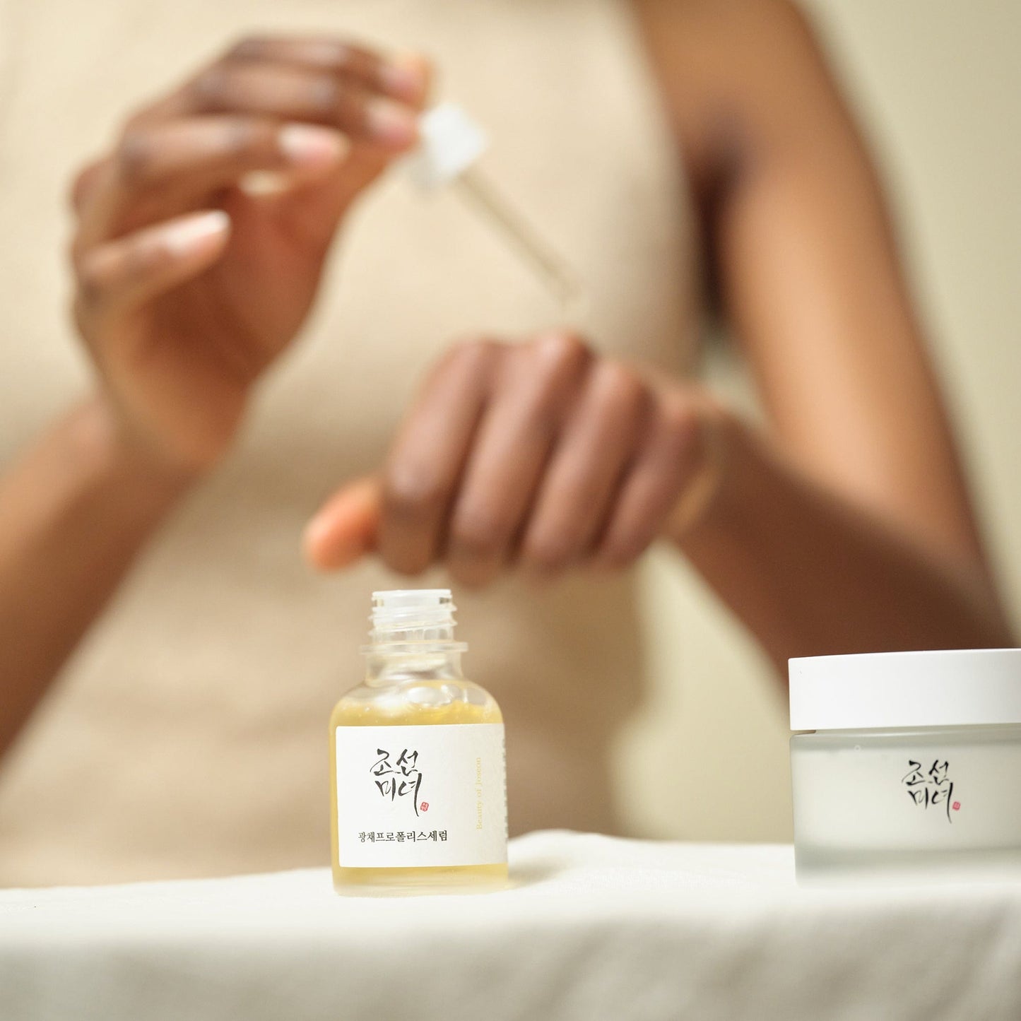 K-Beau models hand applying Beauty of Joseon Glow Serum Propolis & Niacinamide using dropper onto skin for application demo.