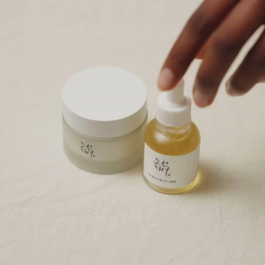 K-Beauty lifestyle image of Beauty of Joseon Glow Serum Propolis & Niacinamide bottle next to matching cream jar with hand reaching.